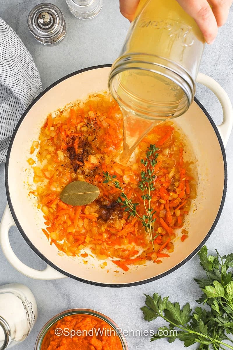 adding broth and herbs to cooked vegetables to make Pumpkin Soup