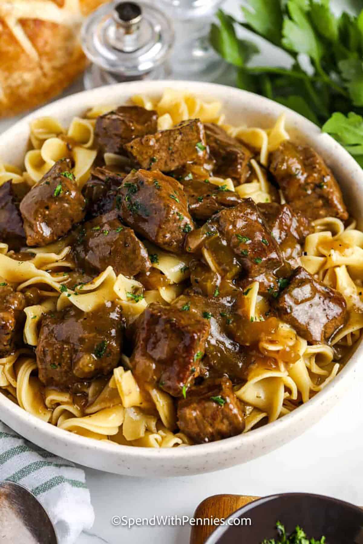 This beef and noodles recipe delivers the best in comfort food with beef, onion, celery, and noodles. The beef is simmered until tender, then coated in savory gravy and served over egg noodles. A sprinkle of parsley brightens the dish, making it fresh and delicious. This recipe is easy enough for a weeknight yet cozy enough for weekends. Add broccoli for a wholesome finish that rounds out the plate. #spendwithpennies bowl of Beef and Noodles Recipe