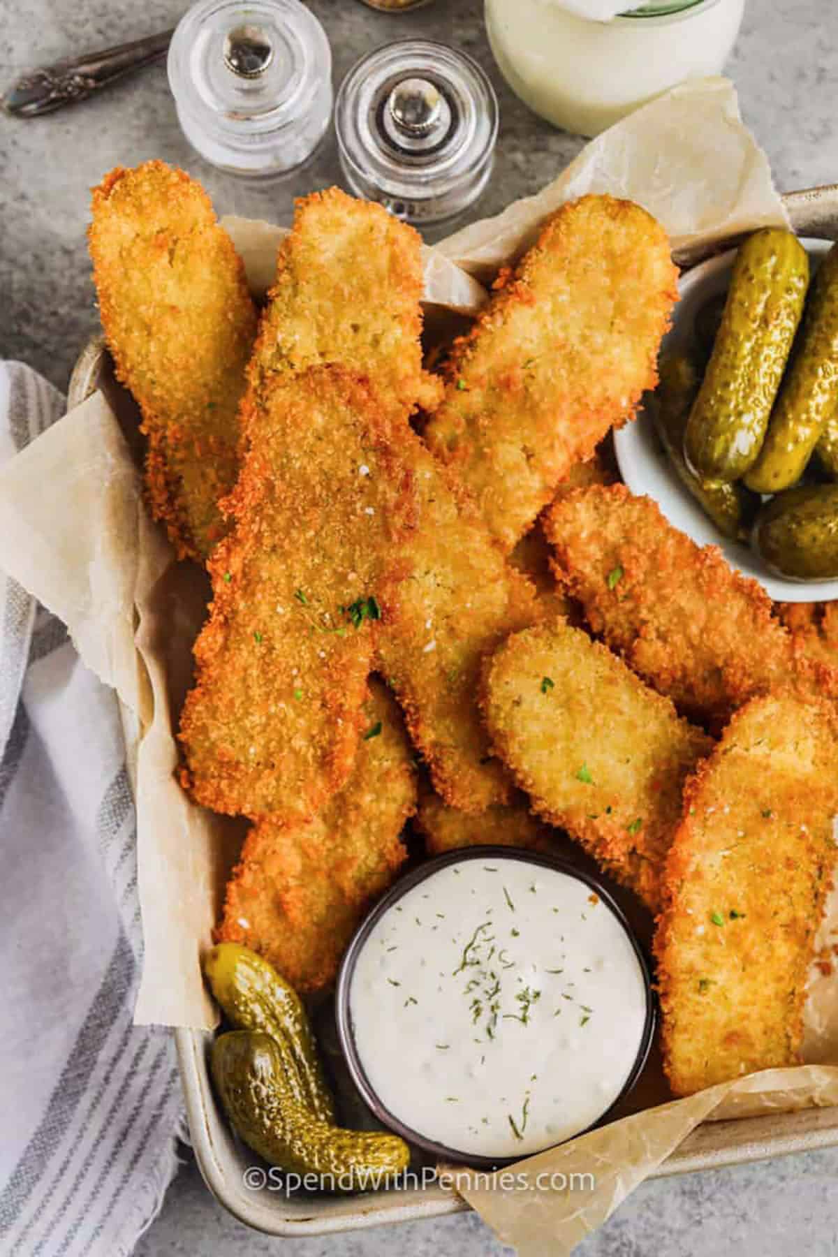 Fried pickles are a crowd-pleasing recipe that combines tangy dill slices with a golden, crunchy coating. The batter and crumb combo make each bite perfectly crisp and flavorful. Dip them into ranch dip or spicy sauce, or serve them on the side with chicken tenders or sandwiches. You can make them into spears for a bigger bite of dill pickle or chip-style for easy snacking. Fried pickles are the best snack for parties, game nights, or anytime cravings hit. #spendwithpennies basket of Crispy Fried Pickles with pickles on the side