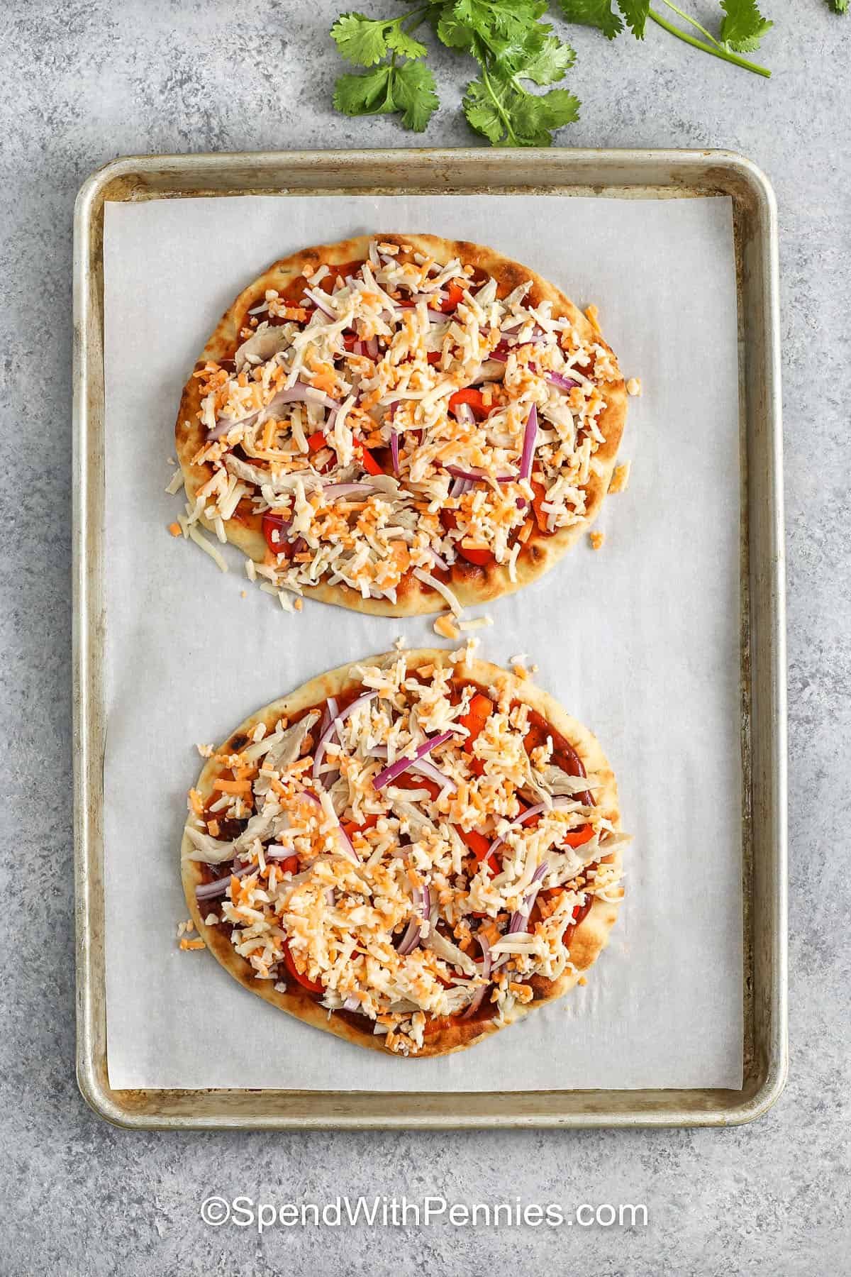 BBQ chicken flatbread makes a quick and delicious meal with just the right balance of nutrition and comfort. A crispy naan bread crust is loaded with shredded chicken, sweet BBQ, and pizza sauce, and melty cheese. Like a tgi friday favorite, but lighter and made at home. Bake, slice, and serve with a side salad for a complete and healthy weeknight dinner. #spendwithpennies BBQ Chicken Flatbread on sheet pan before cooking