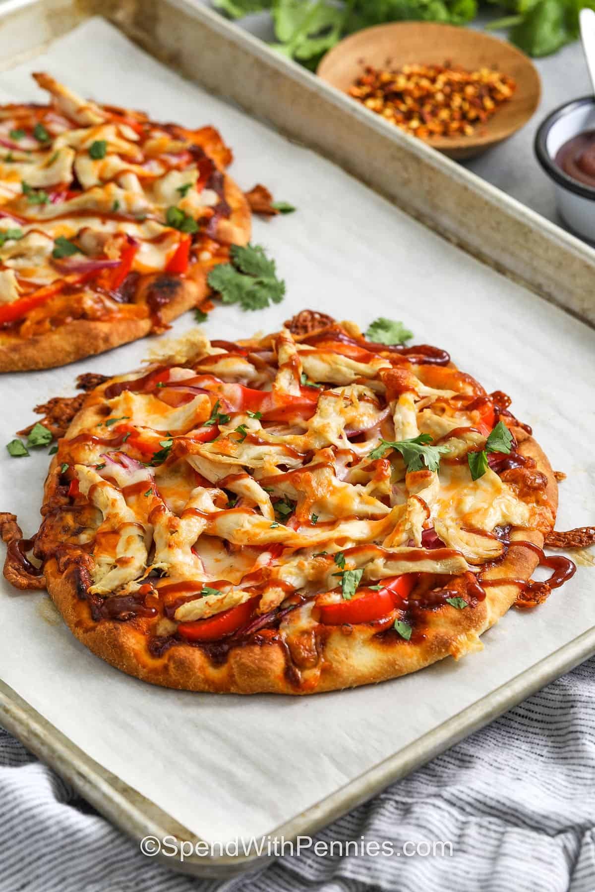BBQ chicken flatbread is the ultimate easy dinner recipe that delivers restaurant-style taste with simple, wholesome ingredients. Think grill-flavored chicken with sweet tropical BBQ sauce, melted cheese, and a crispy base that rivals any Panera flatbread. Top with fresh cilantro and a drizzle of sauce for the perfect finish. Delicious, homemade, and full of feel-good flavor! #spendwithpennies saucy BBQ Chicken Flatbread on a sheet pan