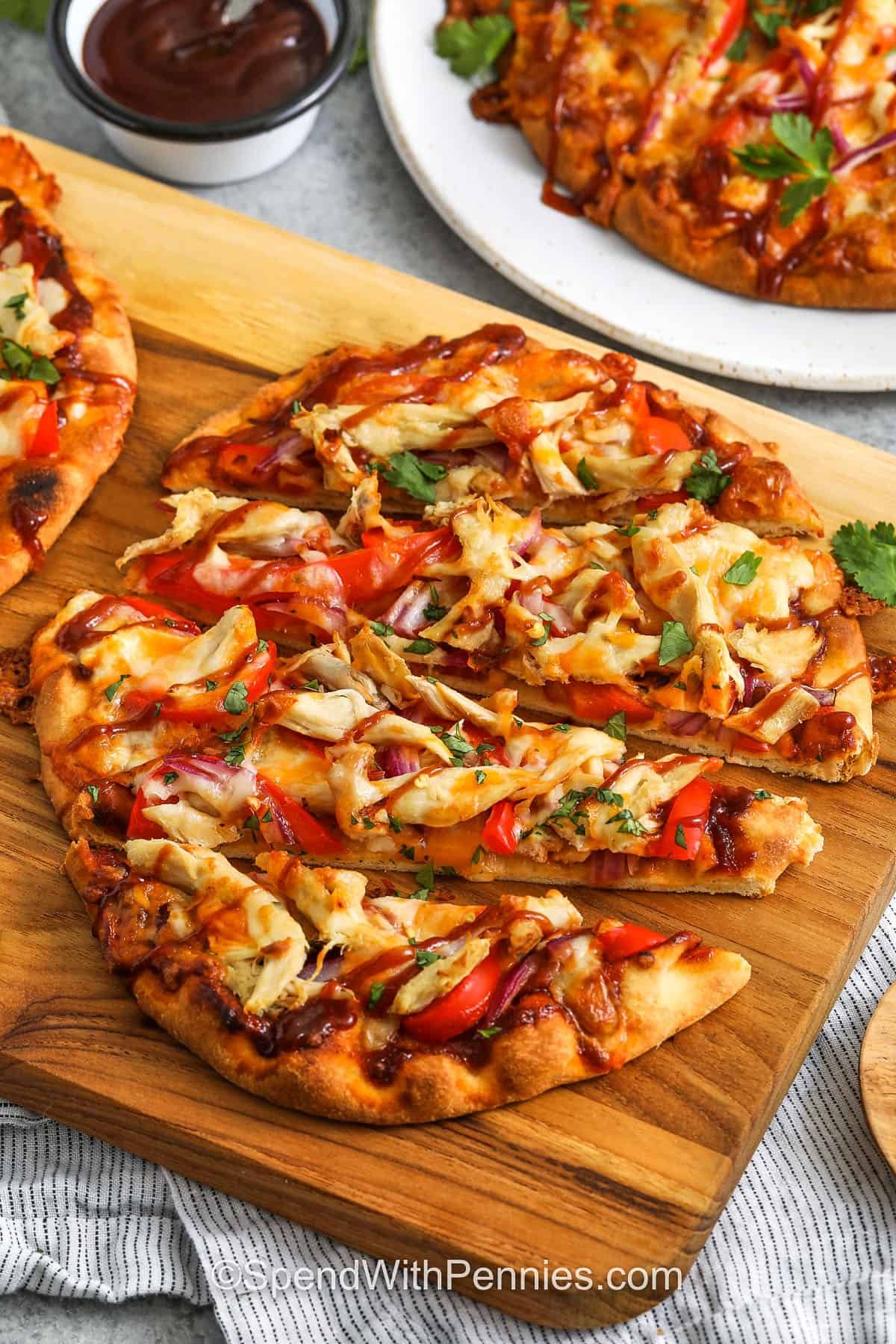BBQ chicken flatbread brings bold flavor without the extra calories, making it a smart and satisfying dinner. Juicy chicken, sweet and smoky BBQ sauce, and gooey cheese sit atop crisp naan bread. It’s like your favorite tgi friday flatbread but fresher, faster, and better for your nutrition goals. Bell peppers and onions give a satisfying crunch that keeps every bite exciting. #spendwithpennies sliced cheesy BBQ Chicken Flatbread