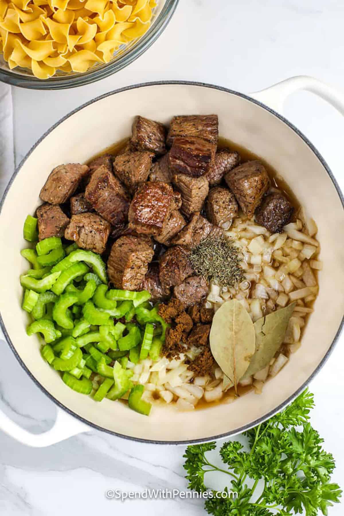 This beef and noodles recipe combines browned beef, onion, celery, and broth with tender egg noodles for a delicious dish that feels like home. Simmered with bay leaves and thyme, the beef is full of flavor and finished in a savory gravy. This easy recipe is hearty enough to be served on its own but pairs well with broccoli or even rice. Simple steps lead to the best kind of comfort food for the dinner table. #spendwithpennies adding ingredients to pot to make Beef and Noodles Recipe