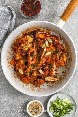 adding green onions on top of Chili Crisp Chicken in the pan