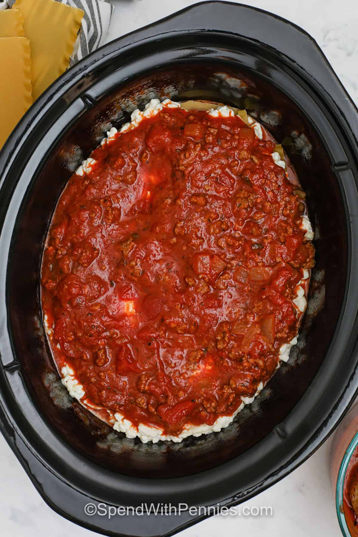 Crockpot lasagna is the easy way to enjoy layers of noodles, seasoned beef, and cheesy ricotta baked into a delicious, hearty meal. This recipe turns a classic favorite into a simple, hands-off dinner your family will crave. Slow cooking makes the sauce rich and the cheese perfectly melted. Add a side of salad or soup for a full meal that everyone will love. #spendwithpennies adding meat sauce layer to pot to make Crockpot Lasagna