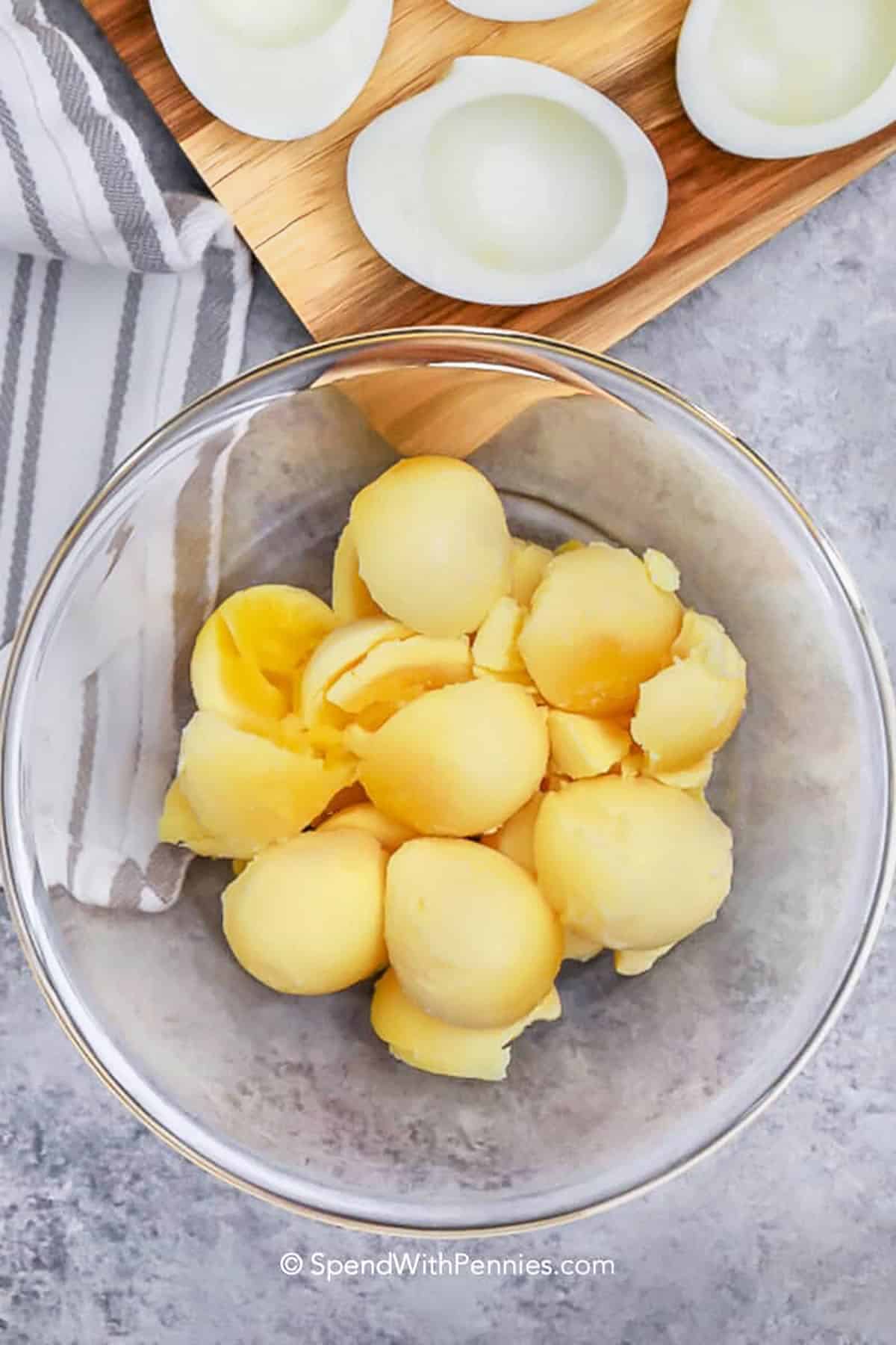 For a tried-and-true deviled eggs recipe, this creamy and tangy version is a must. Boiled eggs are filled with a smooth mixture of mayonnaise, mustard, and vinegar, then topped with paprika or bacon for the perfect bite. It is ideal for brunches, family meals, or holiday celebrations. You can also pair it with fresh fruit or a light salad for a complete appetizer spread. #spendwithpennies adding egg yolks to bowl to make Deviled Eggs