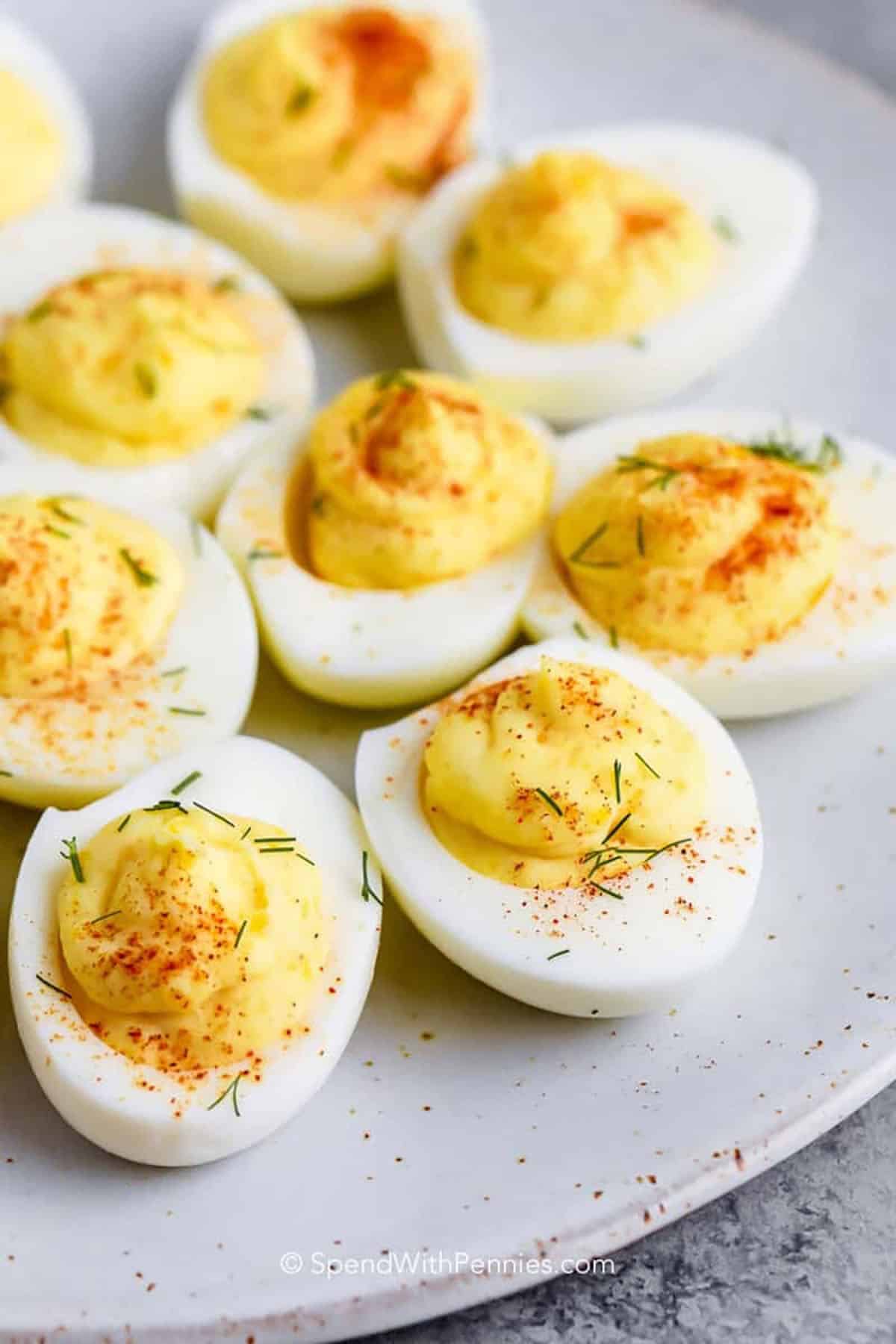 For a tangy deviled eggs recipe that everyone will love, this version is easy and flavorful. The yolks are blended with mayonnaise, mustard, and vinegar, then finished with paprika or crumbled bacon. It makes a beautiful and tasty appetizer for any gathering. Serve alongside fresh vegetables or a cheese platter to elevate the presentation. #spendwithpennies close up of Deviled Eggs on a plate