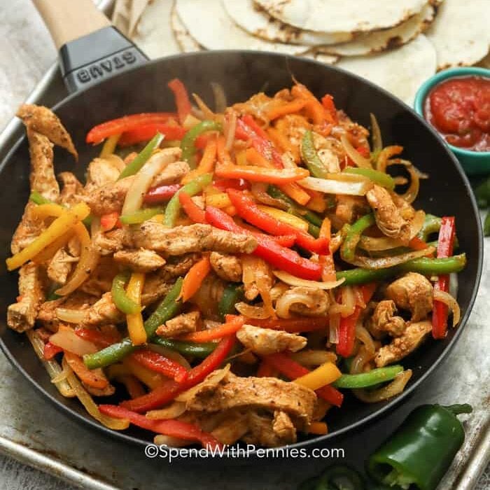 A pan of steaming chicken fajitas with tortillas on a pan with salsa and bell peppers