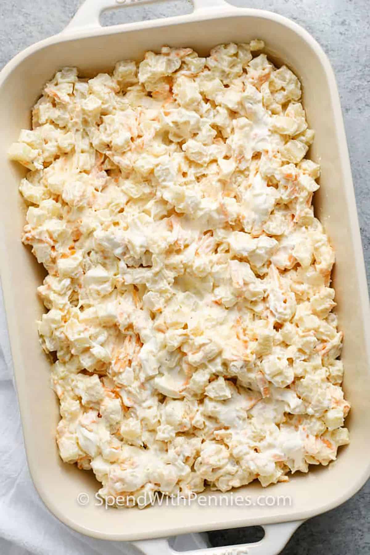 This easy funeral potatoes recipe is pure comfort in every spoonful. Frozen hash browns are baked in a creamy, cheesy sauce that melts into a golden, bubbly casserole. You can cook it in the oven or make it ahead in your crock pot to keep warm for serving. The crunchy topping makes it irresistible. These cheesy funeral potatoes are one dish everyone will go back for seconds on. #spendwithpennies adding ingredients to dish to make Funeral Potatoes