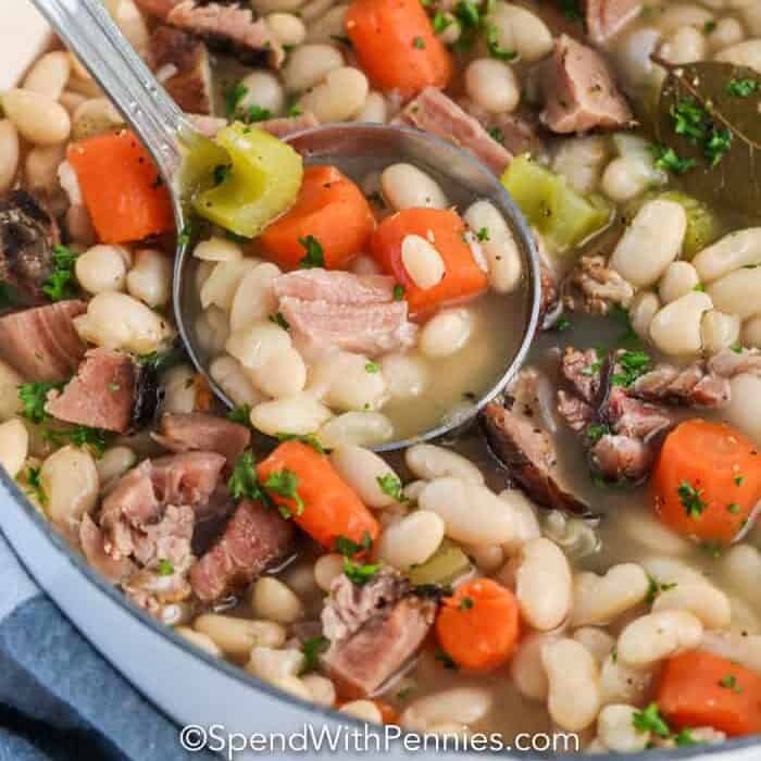 Great Northern beans and ham in a pot with some being scooped out with a ladle