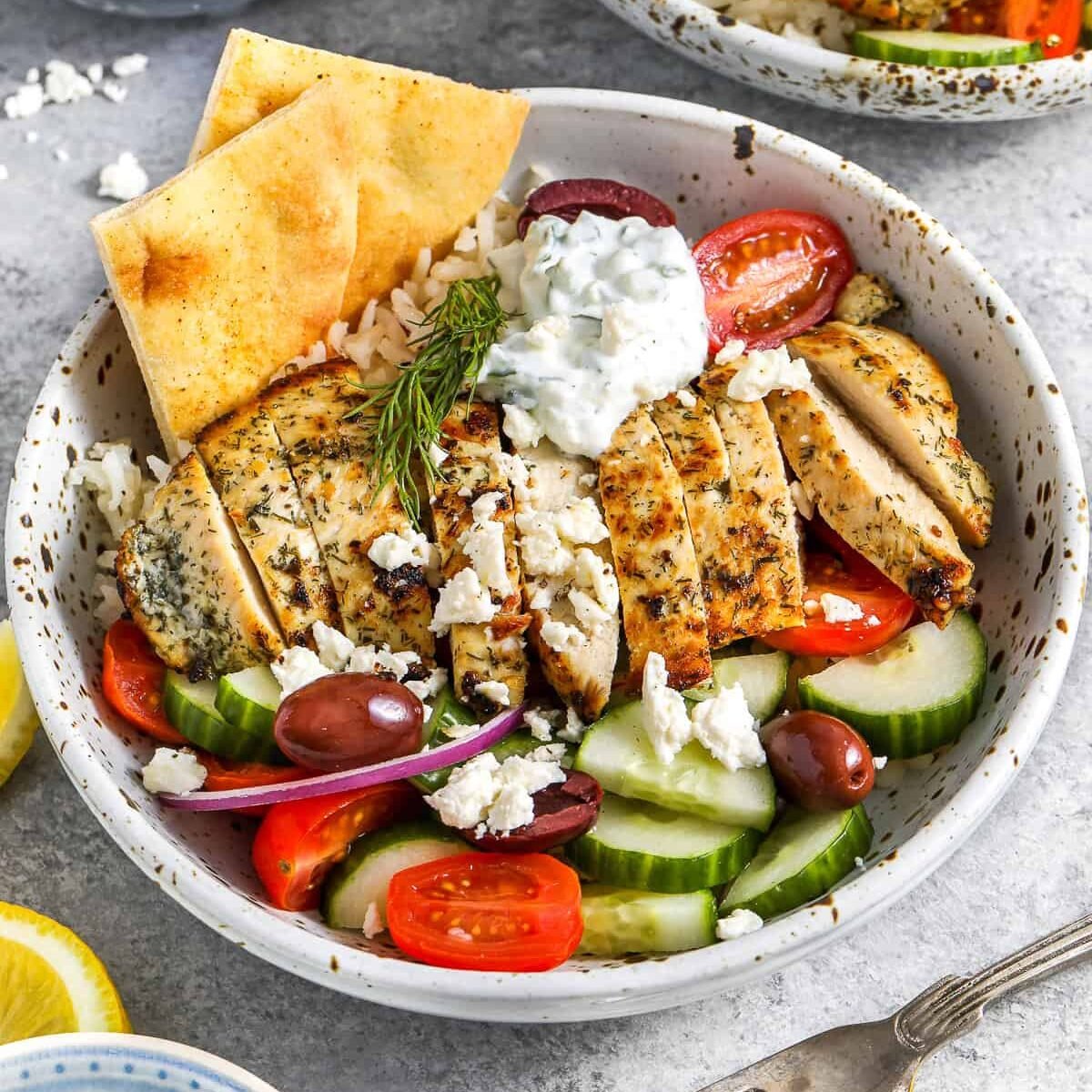 A Greek chicken bowl topped with feta cheese and served with fresh vegetables