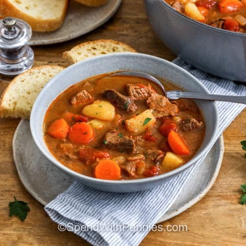 bowls of Hungarian Goulash with a pot full in the back and bread on a plate