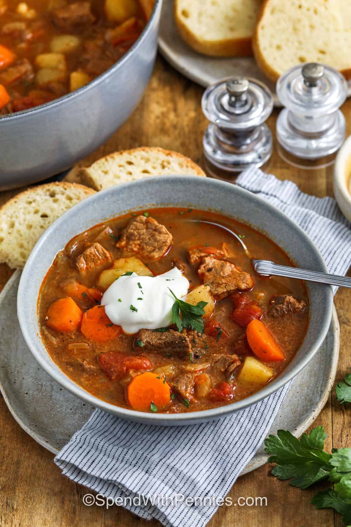 Hungarian goulash is a traditional beef recipe with a rich paprika-spiced broth that’s cozy and full of flavor. Tender beef and vegetables simmer together to create a hearty, filling dish that’s perfect for family dinners. Try it as a soup-style meal with crusty bread or serve over noodles for comfort in every bite. #spendwithpennies bowl of Hungarian Goulash with sour cream on top