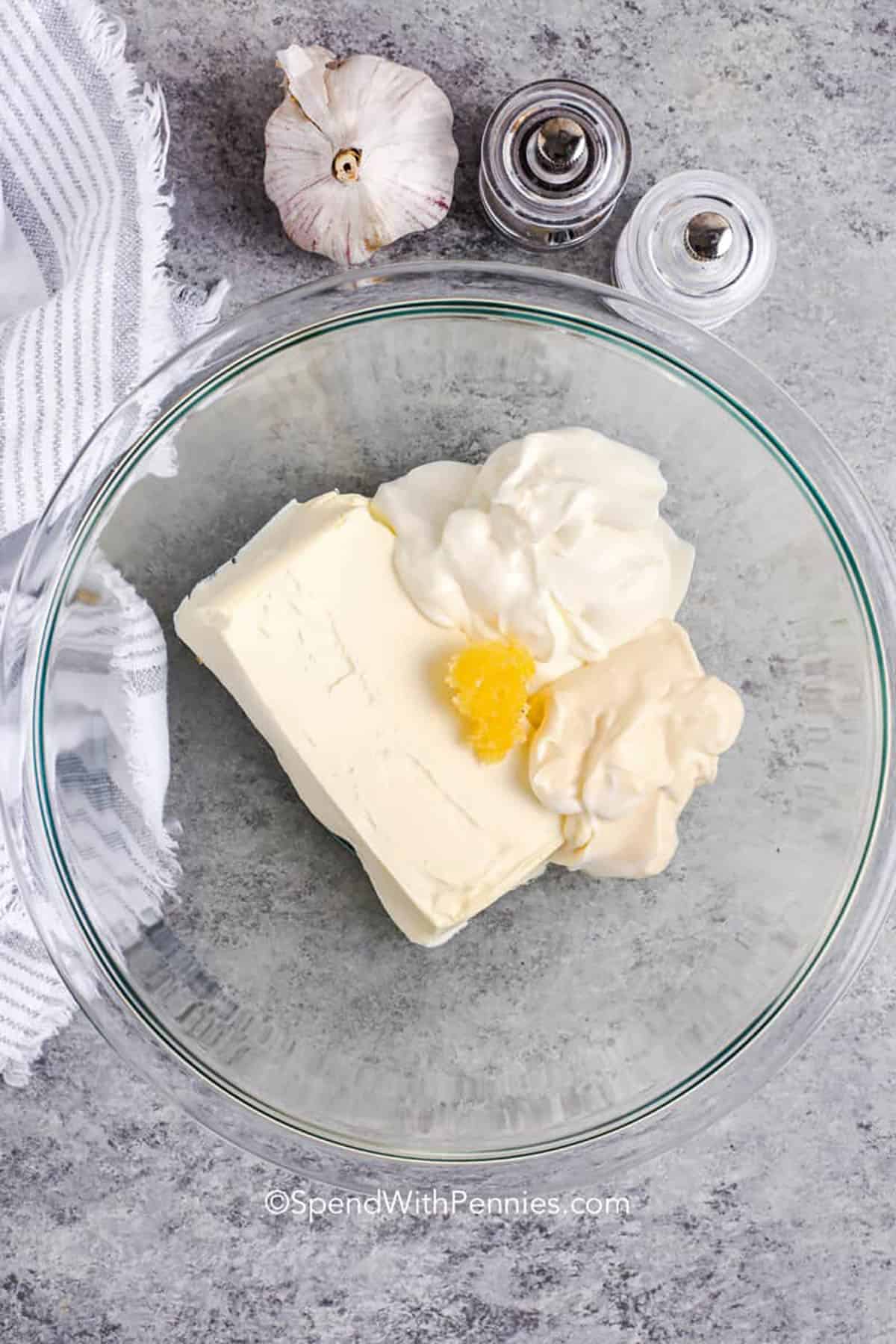 Spinach artichoke dip is rich, creamy, and full of cheesy flavor. This easy recipe blends cream cheese, sour cream, and gooey melted cheese with spinach and marinated artichokes for a warm, comforting appetizer everyone loves. Perfect for dipping bread, chips, or veggies, it’s simple to make and always disappears fast at parties. You can even bake it in a small pot or skillet for easy serving. #spendwithpennies ingredients to make spinach artichoke dip in a bowl with salt and pepper and garlic beside it