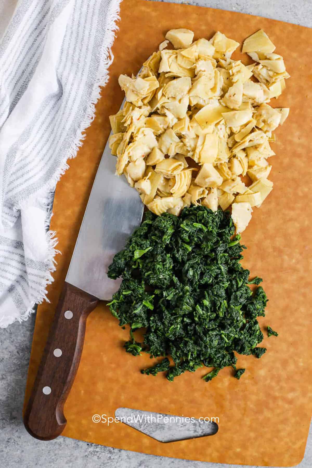 Make this spinach artichoke dip for a warm, cheesy snack everyone will love. It’s full of rich flavor from cream cheese, sour cream, and gooey melted cheese mixed with tender spinach and chopped artichokes. Serve it hot and creamy with bread, crackers, or even pita chips for dipping. So simple and so good. #spendwithpennies chopped spinach and artichokes on a cutting board with a knife for spinach artichoke dip