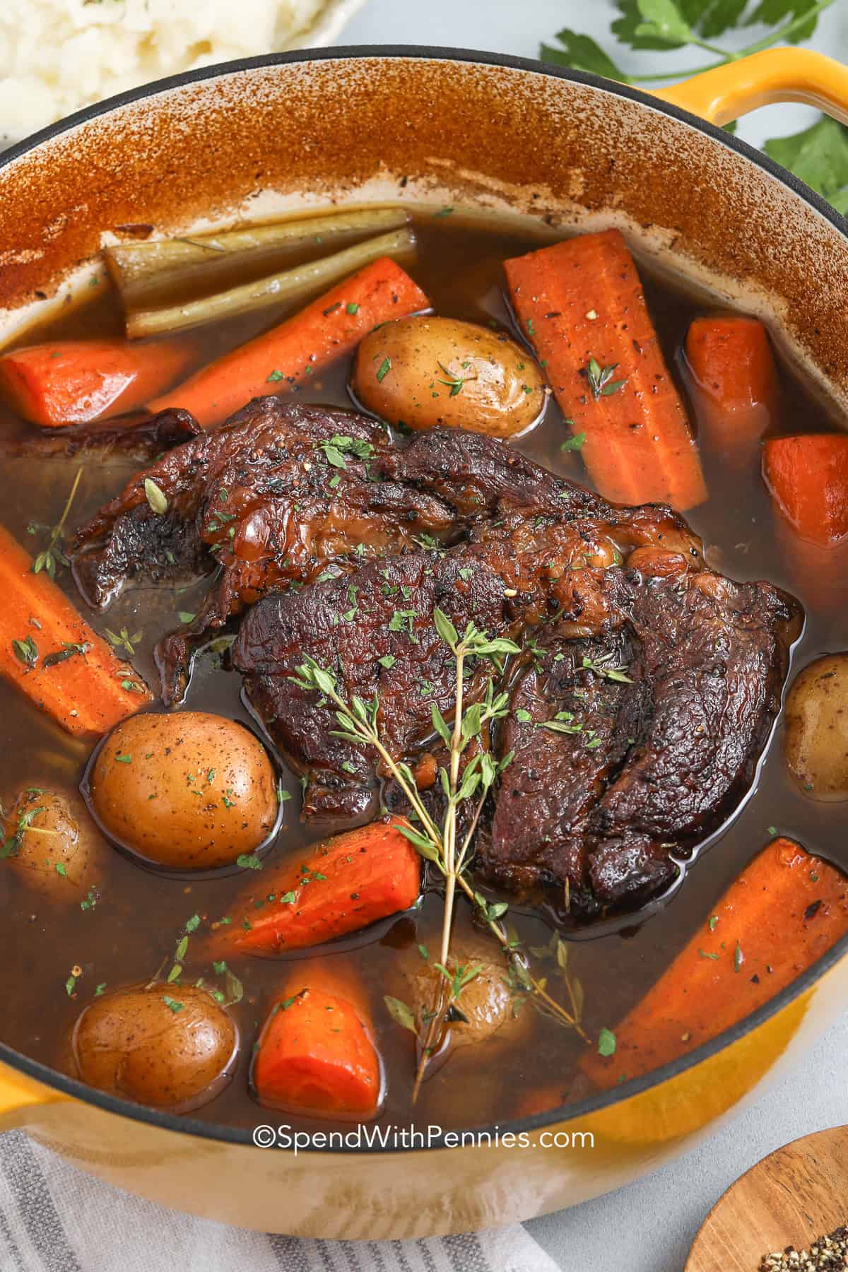 a cooked pot roast in a pot with thyme, carrots and potatoes