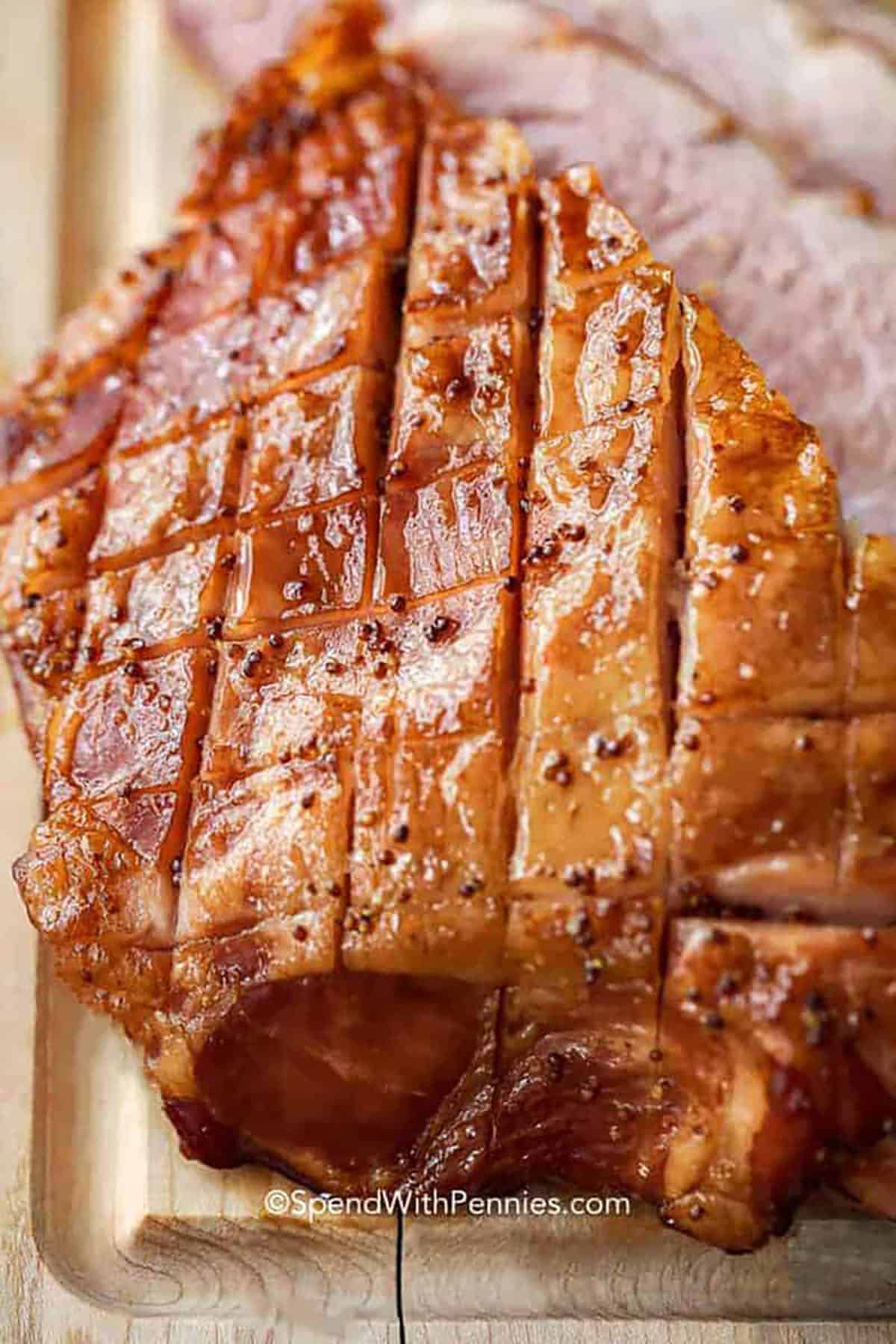 This easy ham glaze blends brown sugar, citrus, Dijon, and a touch of cloves to create a glossy, flavorful coating. It comes together in minutes and adds just the right balance of sweetness and tang. Whether you are preparing a spiral-cut ham or scoring a whole ham, this simple glaze caramelizes beautifully. A reliable favorite for holidays or weeknight dinners. #spendwithpennies ham with The Best Ham Glaze on a cutting board