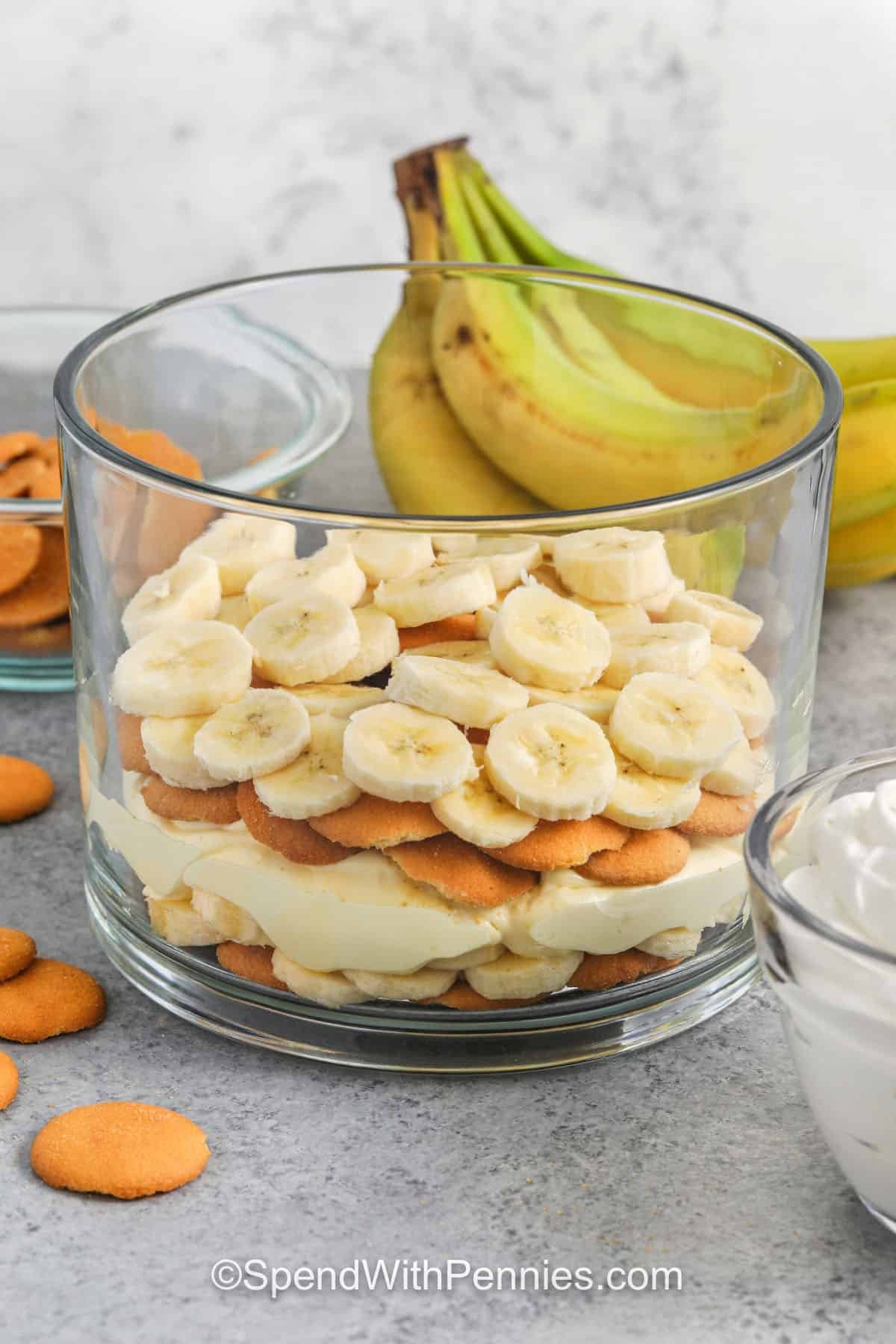 Try this banana pudding recipe for a classic creamy treat made with sweetened condensed cream, layers of vanilla pudding, and fresh bananas. Nilla wafers add the perfect crunch, and a soft whipped topping makes it light and airy. It’s easy to make and great for any gathering. The smooth texture and rich flavor taste like banana cream pie in every spoonful. Cool, creamy, and so good for sharing with family and friends. #spendwithpennies adding layers to dish to make Banana Pudding