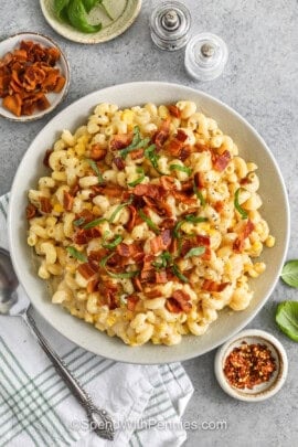 top view of corn pasta with bacon and basil chiffonade on top, small bowls of basil bacon and red pepper flakes and salt and pepper shaker on the side