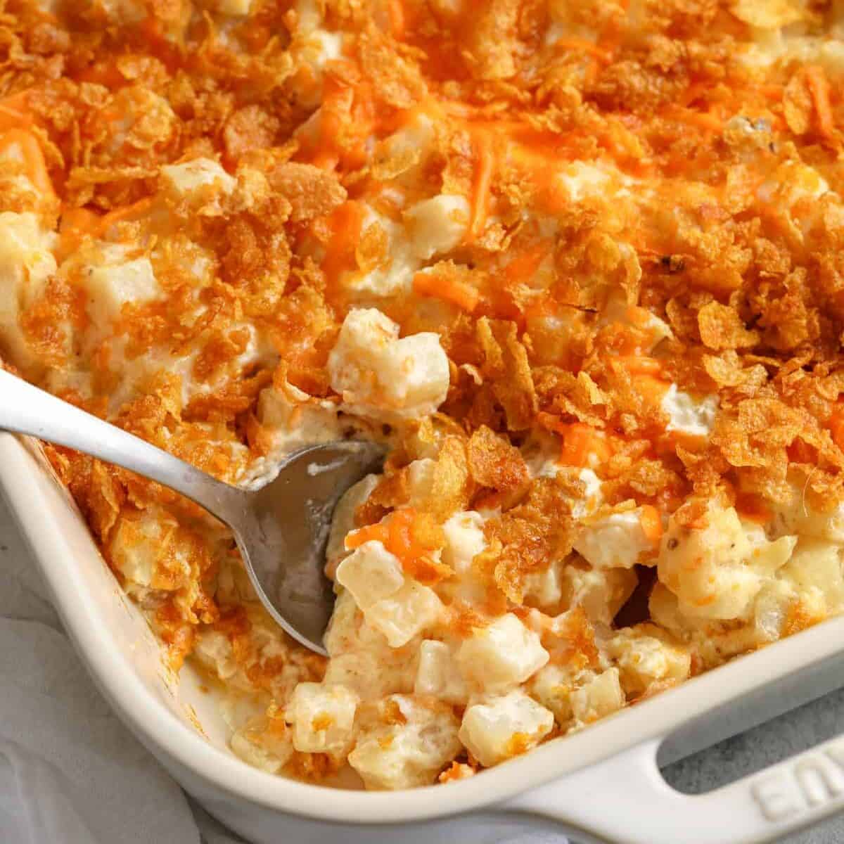 cooked Funeral Potatoes in a white casserole dish with a spoon taking a portion out