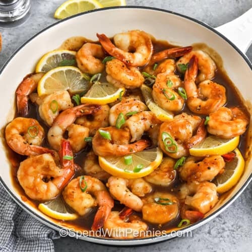 closeup of a pan of honey garlic shrimp with lemon wedges