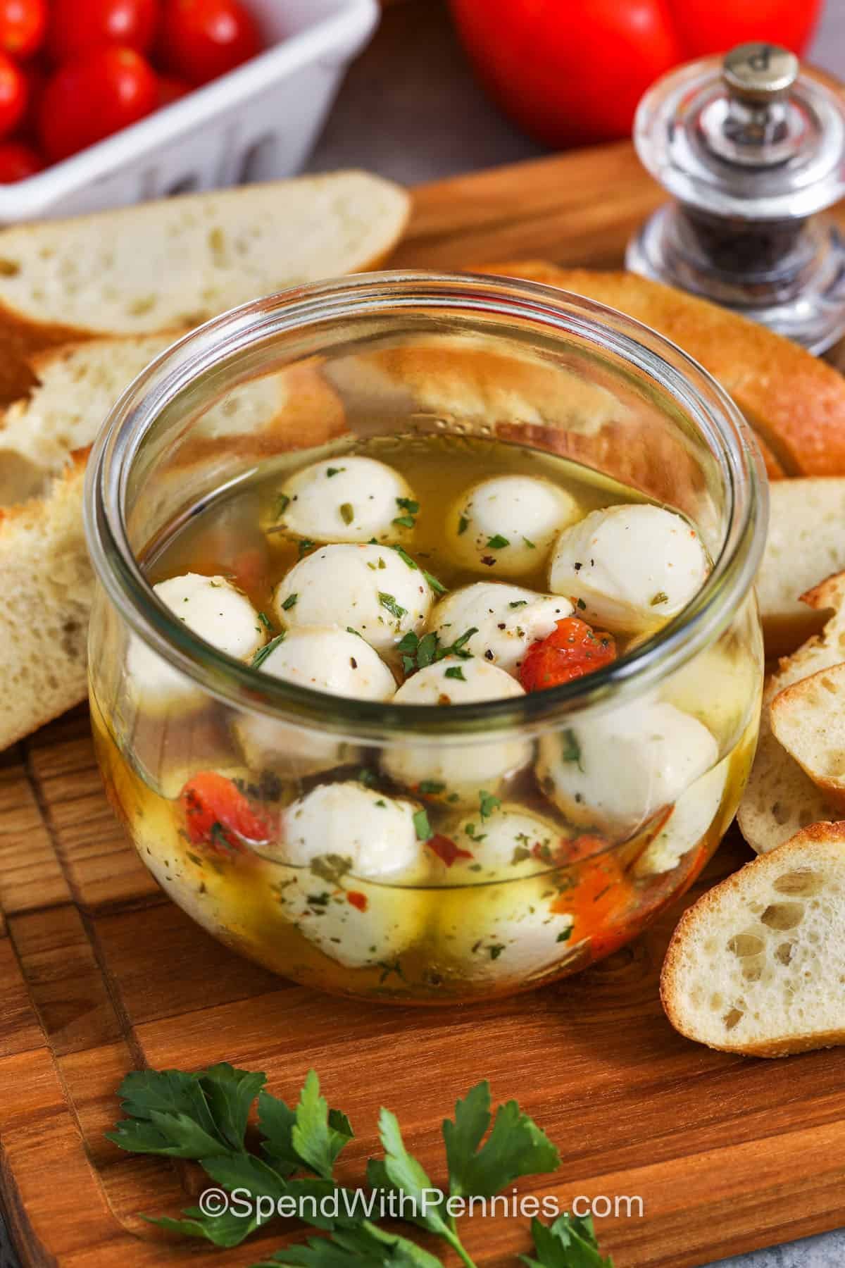 a jar of marinated mozzarella balls on a cutting board with crostini