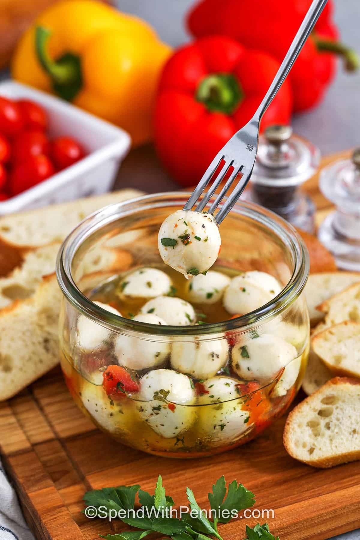 a fork taking a marinated mozzarella ball out of the full jar with crostini and ingredients in background