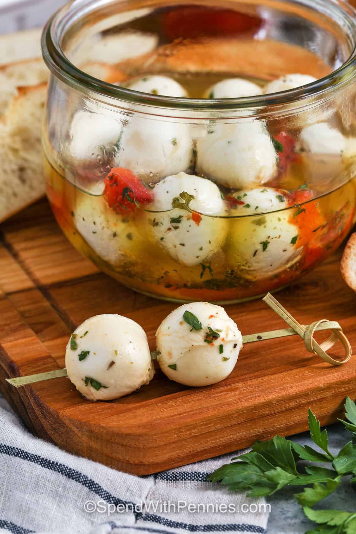 a skewer with two marinated mozzarella balls on it and the full jar in the background