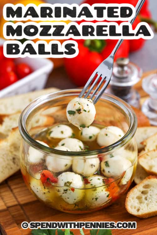 a fork taking out a marinated mozzarella ball from the jar with writing