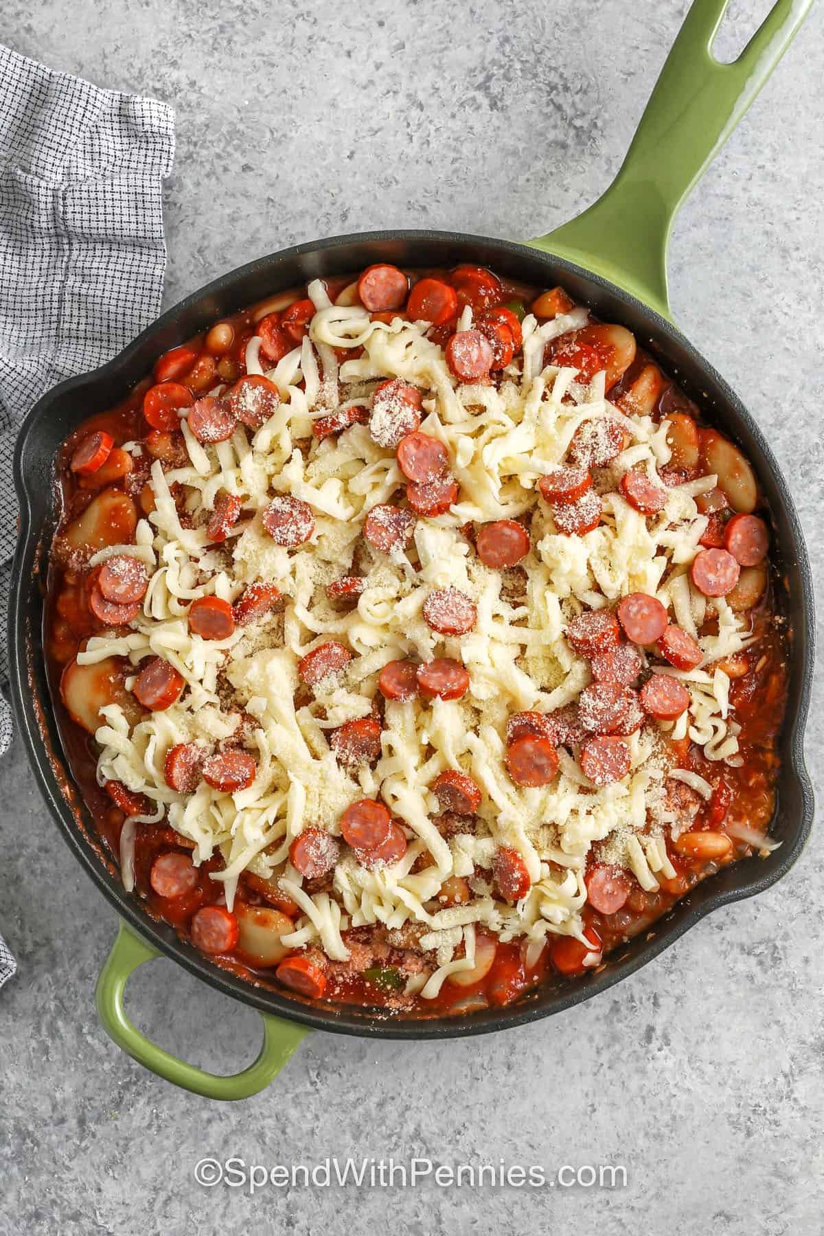 Pizza beans make a hearty family meal with white and butter beans folded into pizza sauce and tomato sauce, along with pepperoni for a boost of savory flavor. The cheese melts into a soft topping that makes every bite warm and creamy. Add black olives or chopped veggies if you want more color. It is great with slices of crusty bread for dipping. #spendwithpennies adding cheese and pepperoni to pan to make Pizza Beans