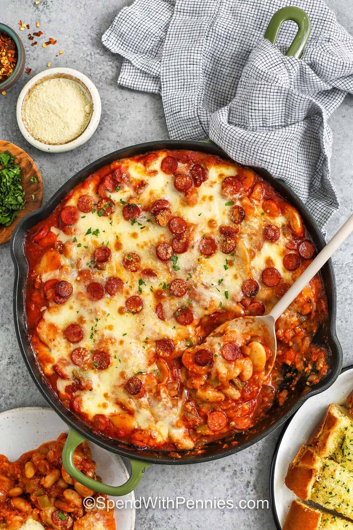 Pizza beans are a simple dish with soft beans mixed with pizza sauce, tomato sauce, and pepperoni that bake together until the cheese turns lightly golden. The skillet smells cozy and full of flavor. Add black olives or spinach if you want a little more color or crunch. Warm bread or focaccia makes it extra tasty. #spendwithpennies Pizza Beans in the pan with a spoonfull