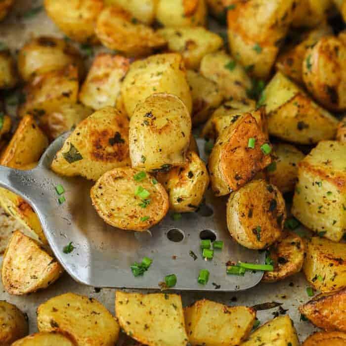 Using a spatula to lift o ut Oven Roasted Potatoes from baking sheet