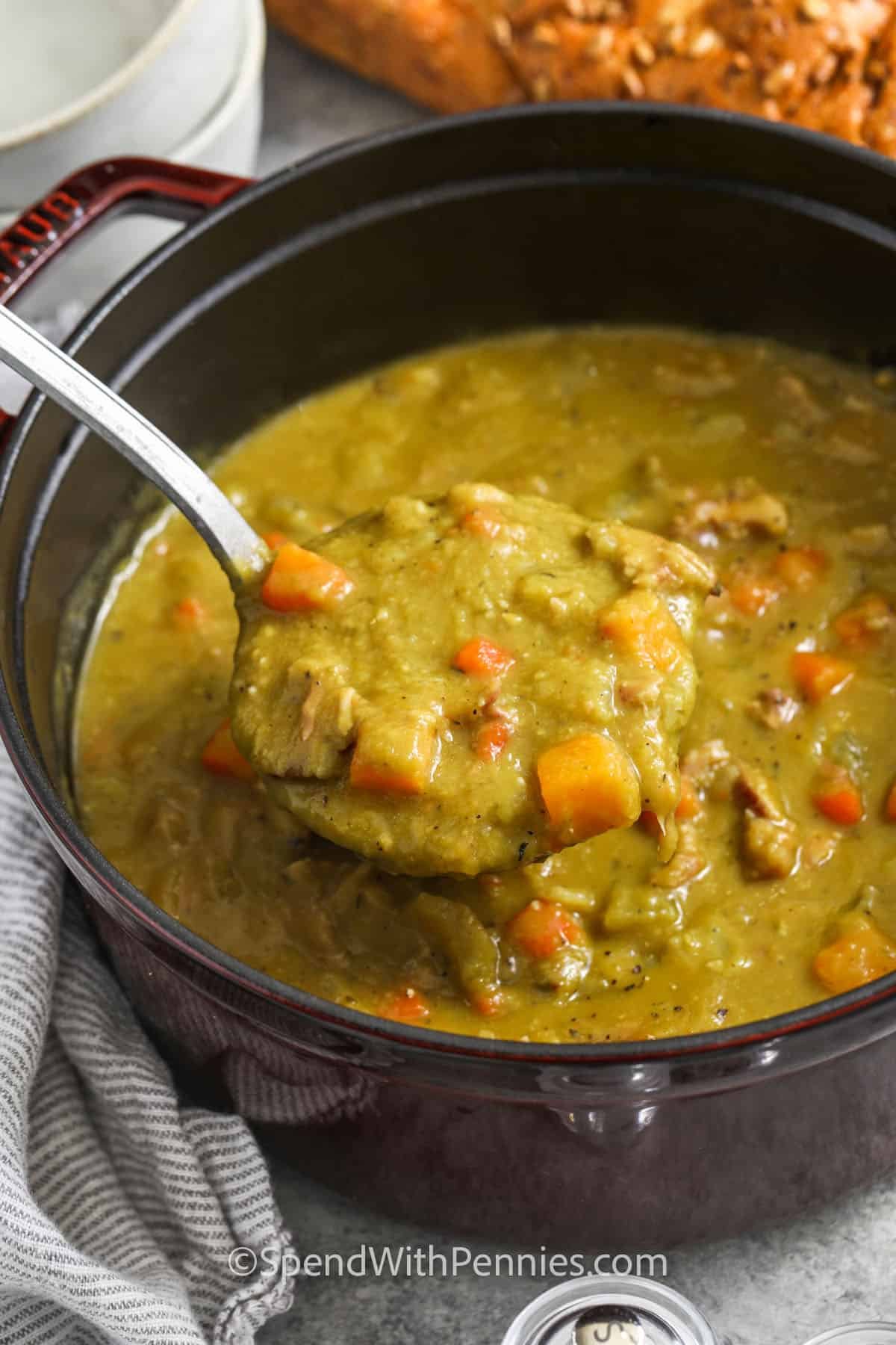 Split pea soup turns leftover ham and pantry staples into a creamy, comforting meal that’s ideal for cold days. Slow-simmered with split peas, carrots, celery, onion, and herbs, it thickens naturally and delivers smoky, savory flavor in every spoonful. This easy, one-pot recipe is freezer-friendly, perfect for meal prep or quick weeknight dinners, and makes a satisfying, homemade alternative to canned soup that the whole family will love. #spendwithpennies A ladle of split pea soup in a large dutch oven