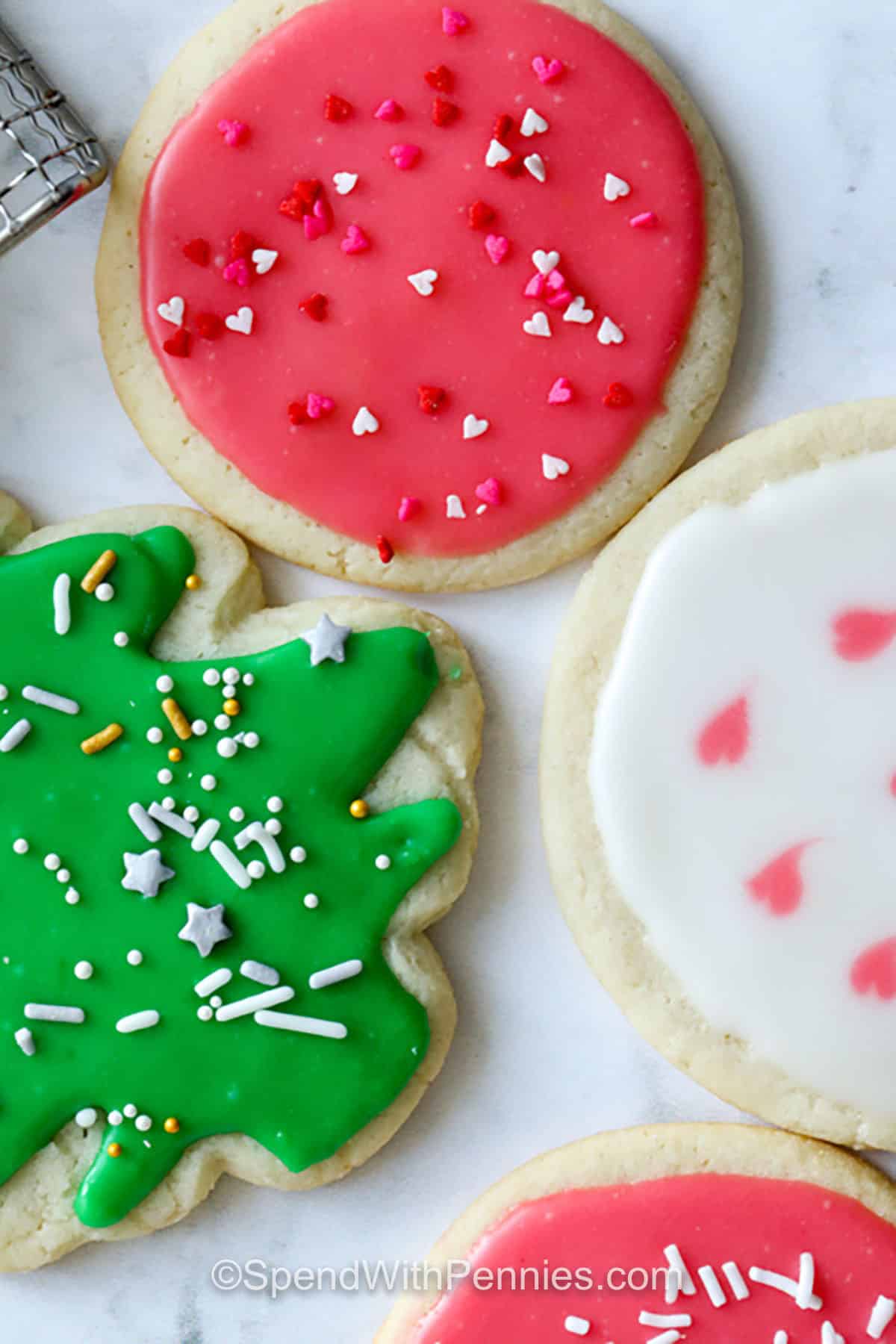 This sugar cookie icing recipe creates a smooth, glossy finish with powdered sugar, clear vanilla, and corn syrup. It is easy to adjust for outlining or flooding, and gel food coloring gives vibrant hues without thinning the icing. Perfect for holiday cookies, this icing dries firm enough for stacking while staying soft to bite. #spendwithpennies red , green and white Sugar Cookie Icing on cookies with sprinkles
