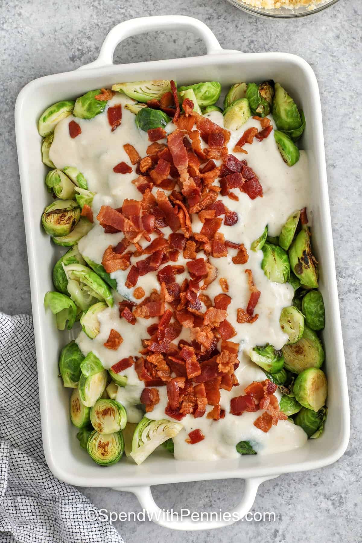 Bring rich holiday comfort to the table with this creamy Brussel sprout casserole. The cheese sauce melts smoothly over tender sprouts, and the bacon adds a smoky touch that complements the buttery topping. This casserole fits perfectly beside classic Christmas mains and is easy to make ahead. Its cozy flavors make it a favorite for winter gatherings. #spendwithpennies adding sauce and bacon to brussel sprouts to makeBrussels Sprout Casserole