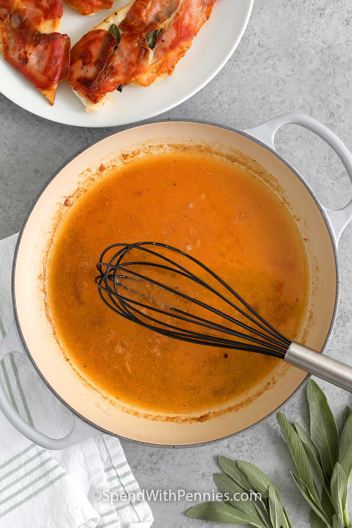 white wine and butter sauce in a skillet with cooked chicken saltimbocca on a plate off to the side