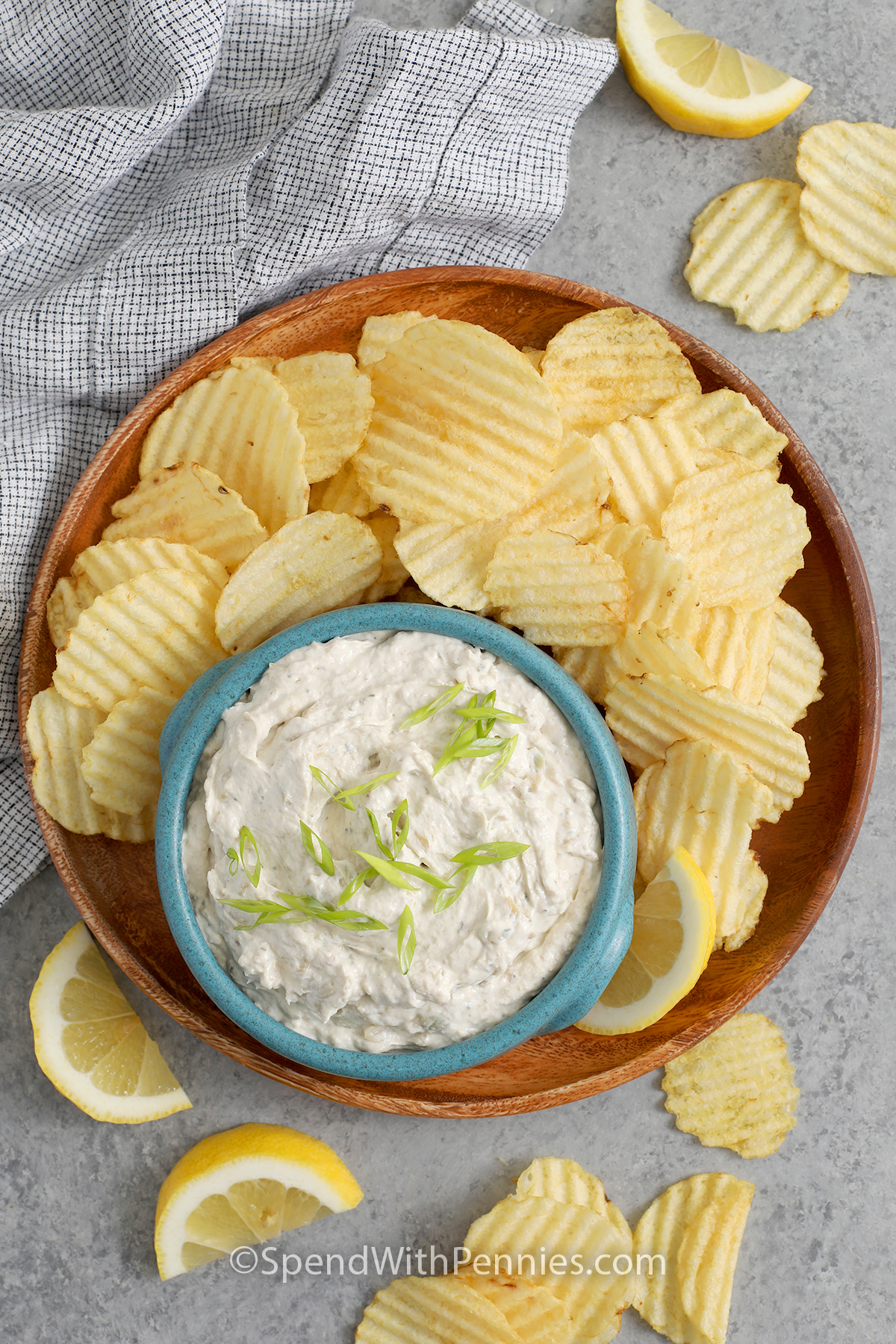 Clam dip in a bowl on a plate of wavy potato chips garnished with green onion and lemon slices.