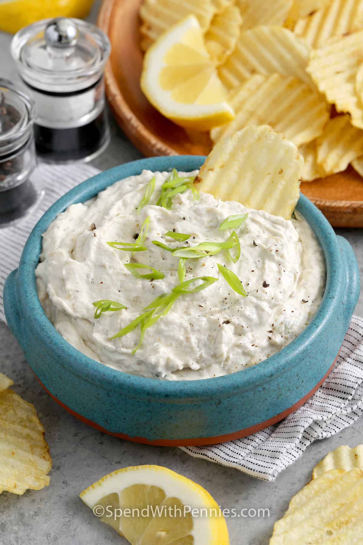 Close up of a bowl of Clam Dip garnished with green onion and chips in the background