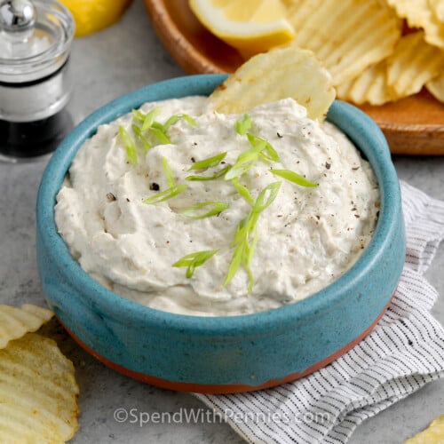 Close up of a bowl of Clam Dip garnished with green onion and chips in the background