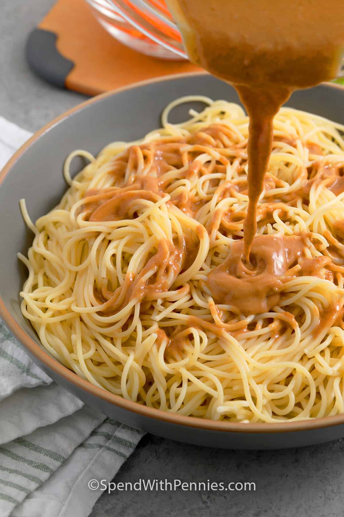 peanut sauce being drizzled over cooked and cooled spaghetti noodles to make cold sesame noodles