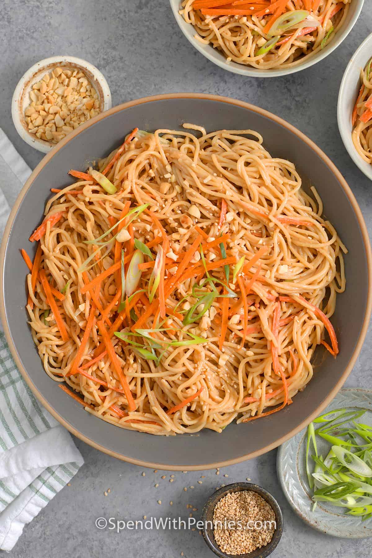 Overhead view of a serving dish of cold sesame noodles topped with matchstick carrots, sliced green onion, sesame seeds and chopped peanuts