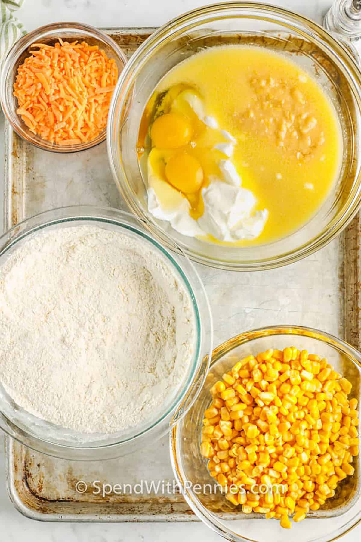 wet ingredients mixed in a bowl with dry ingredients , corn and cheese in seperate bowls to make Cornbread Casserole