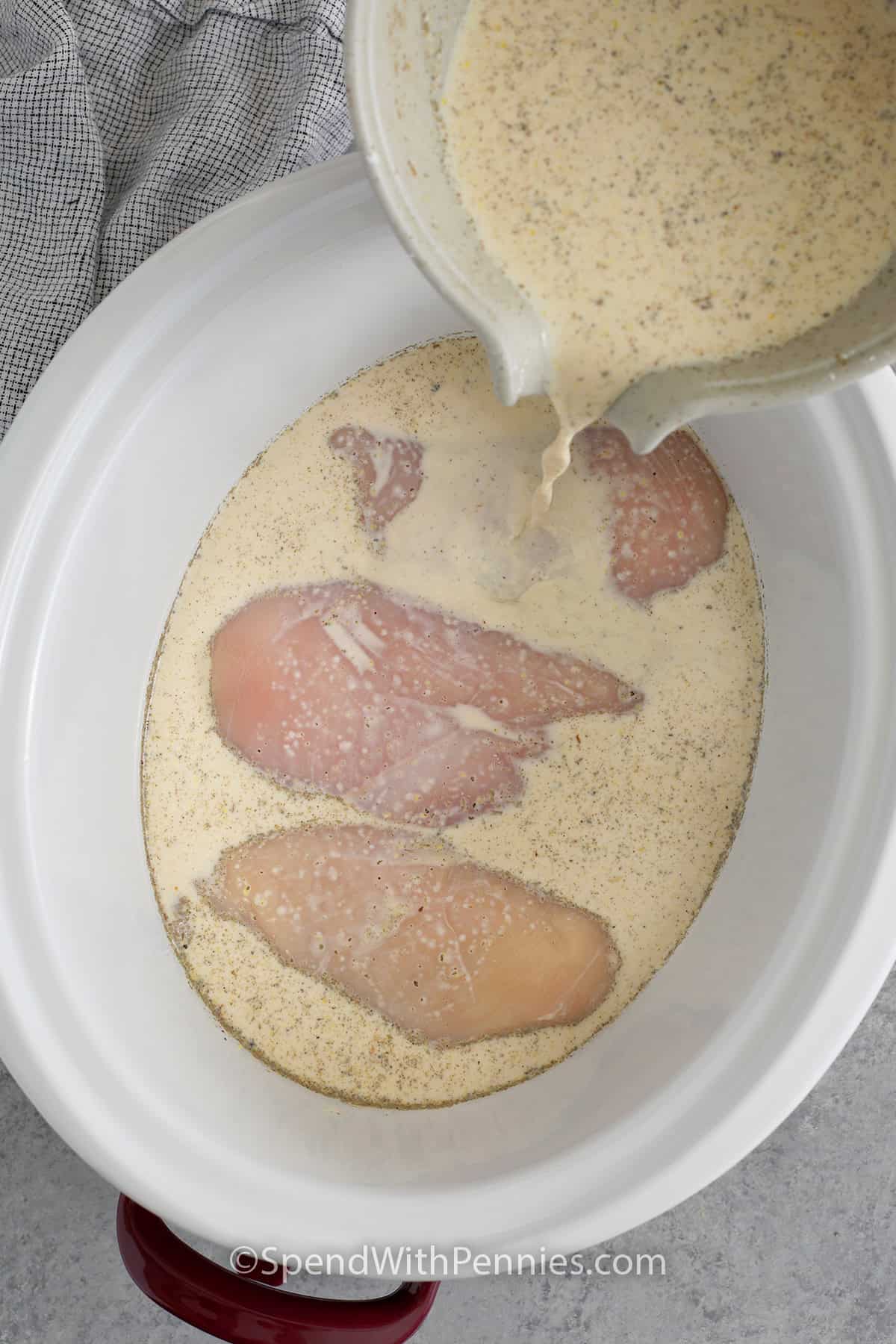 This slow cooker chicken and gravy recipe is great for meal prep because it stores and reheats well. The chicken cooks hands-off, and the gravy thickens at the end so it is not watery. Evaporated milk creates a creamy texture, while onion and garlic powder keep the flavor classic. Serve it over mashed potatoes or buttered noodles and freeze extra portions for later dinners. #spendwithpennies Combined gravy ingredients being poured over chicken breasts in a crockpot