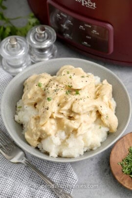 Crockpot chicken and gravy served over mashed potatoes in a bowl and garnished with parsley.