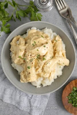 Overhead of crockpot chicken and gravy served over mashed potatoes in a bowl and garnished with parsley.