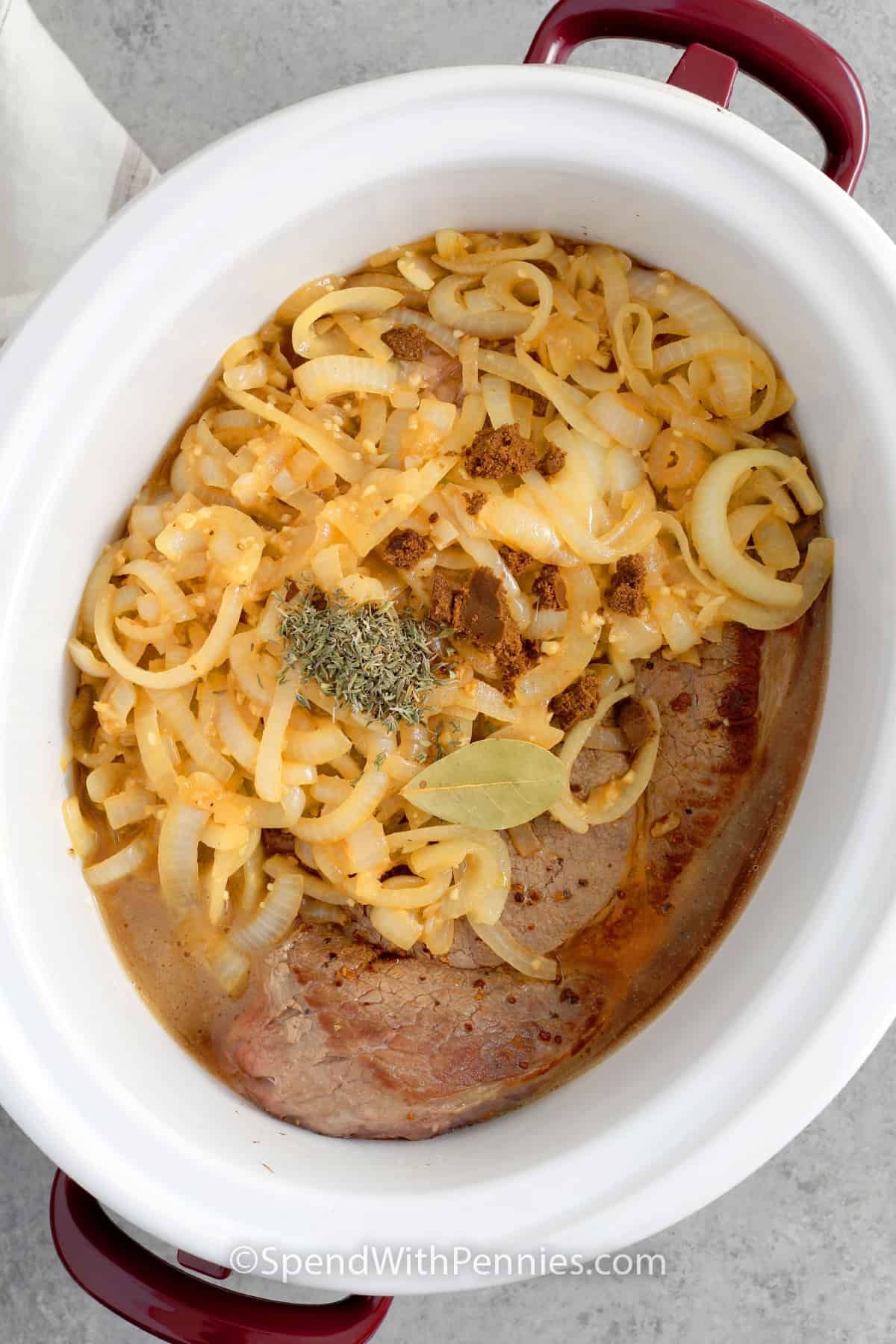 Chuck roast, cooked onions, beef stock, bouillon, thyme and a bay leaf in a crock pot to make French Onion Pot Roast.