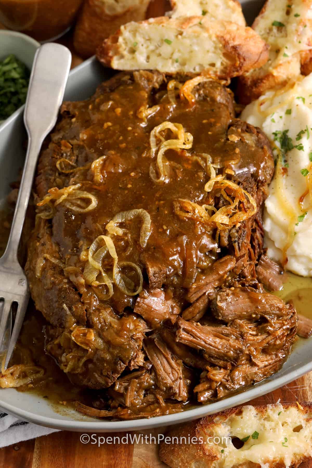 Close up of French Onion Pot Roast on a platter with mashed potatoes and cheese toasts.