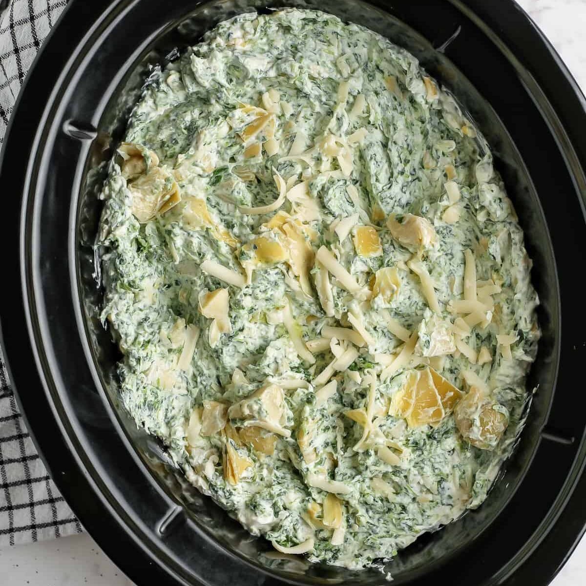 adding cheese to Crock Pot Spinach Artichoke Dip