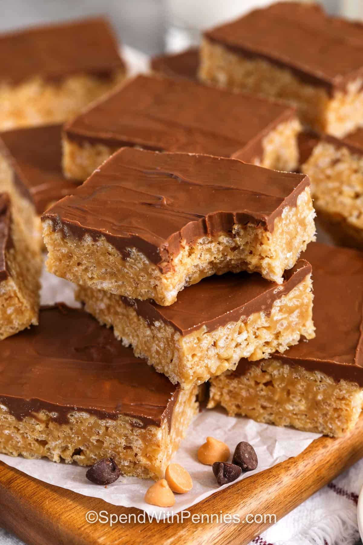 Make a batch of Scotcheroos with simple pantry staples and a few quick steps. A warm peanut butter mixture coats crisp cereal, creating a chewy base that pairs perfectly with the smooth chocolate-butterscotch topping. These bars are great for entertaining because they travel well and stay soft for days. Their classic flavor and easy preparation make them a favorite for busy families. #spendwithpennies Scotcheroos and a bite taken out of one