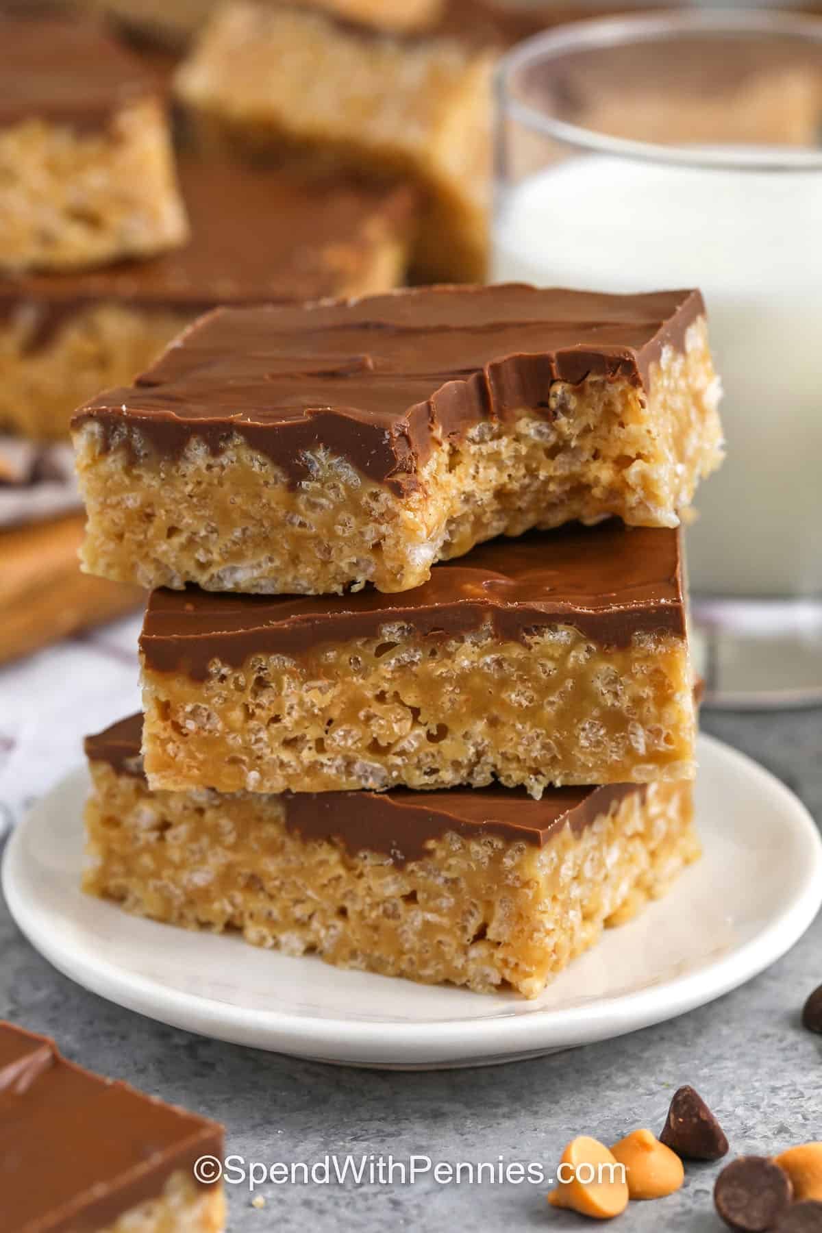 This Scotcheroos recipe creates soft, chewy cereal bars coated in a silky blend of chocolate and butterscotch. The peanut butter syrup comes together quickly on the stovetop and mixes easily with crisp cereal for a perfect texture. These bars are ideal for potlucks, bake sales, or simple weeknight treats. They set beautifully and slice cleanly, making them a reliable no-bake dessert for any occasion. #spendwithpennies Scotcheroos in a stack with a bite taken out of the top one